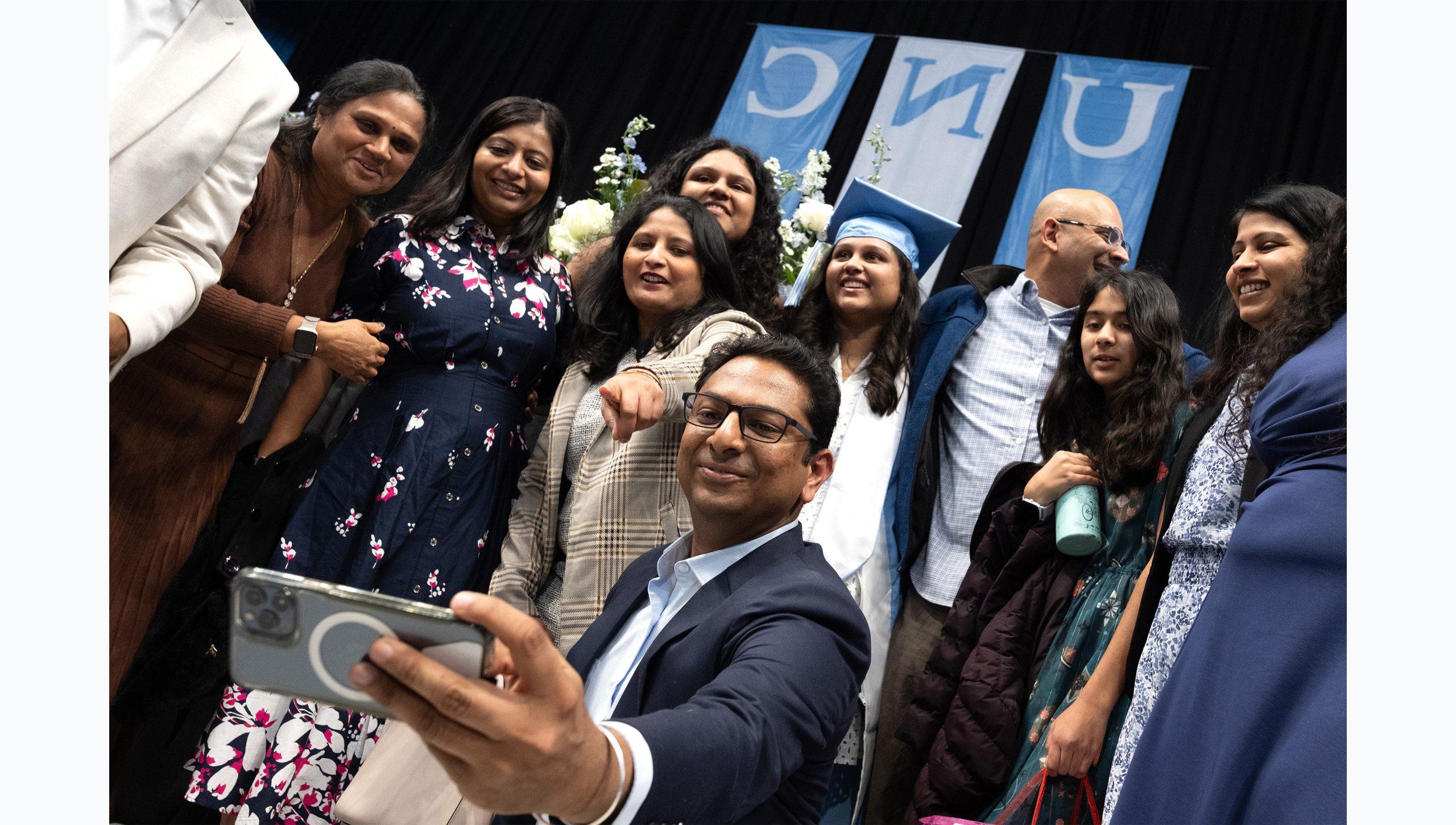 A graduate surrounded by her family, including one man who's taking a group selfie on a phone at U.N.C. Chapel Hill's Winter Commencement.