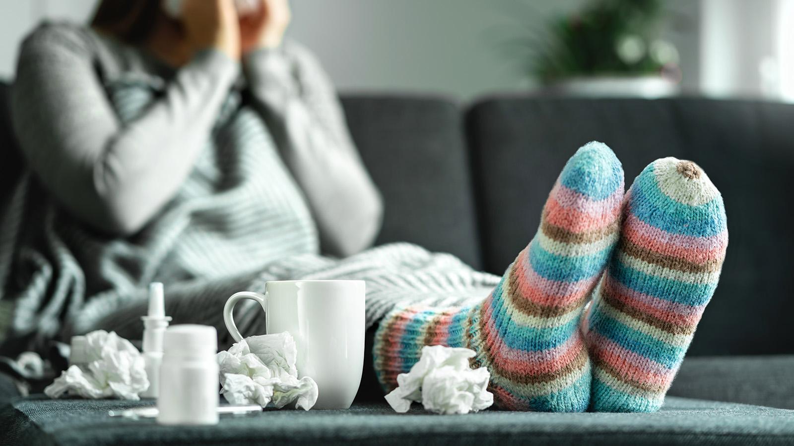 Individual sitting on couch wearing socks, feet on the table, surrounded by tissues.